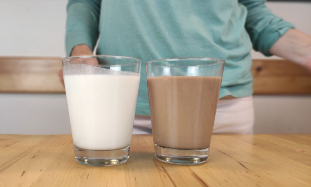 como hacer leche de amaranto casera un vaso con leche de amaranto blanca y otro vaso con leche de amaranto y cacao de color chocolate reposan sobre una mesa de madera
